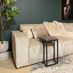 Luxueuze beige bank met zachte kussens en een modern zwart salontafeltje in een stijlvolle woonkamer met groene muur en kunstwerk.