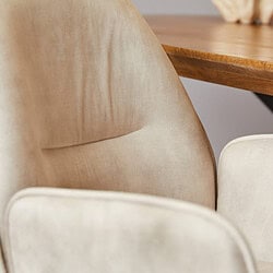 Gepolsterde, beige eetkamerstoel met stoffen bekleding en houten tafel in een modern interieur.