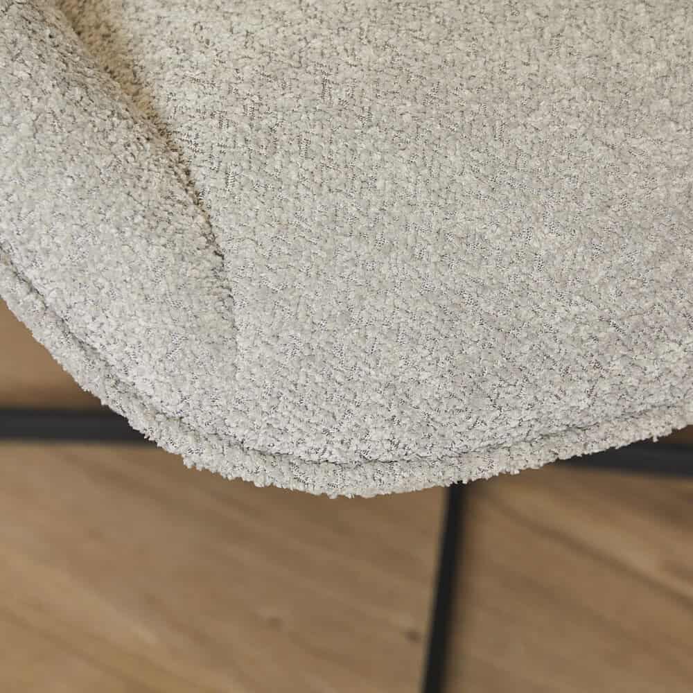Moderne beige stoffen fauteuil met zwarte metalen pootjes, naast een houten vloer, perfect voor een eigentijdse woonkamer stijl.