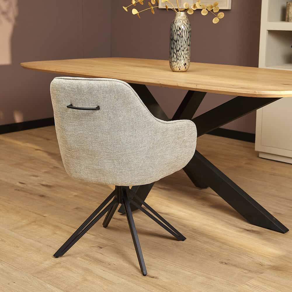 Modern eetkamerstoel met lichtbeige stoffen bekleding en zwart metalen poot onder een eikenhouten eettafel, stijlvol en comfortabel design.