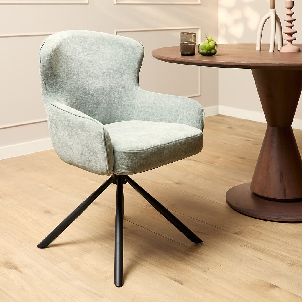 Zweef fauteuil met lichte groene bekleding op zwart metalen poten, modern meubelstuk in een stijlvolle interieur setting.