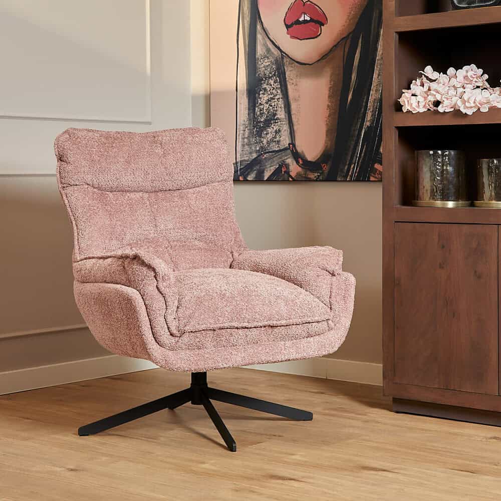 Zachte roze fauteuil met draaibaar onderstel in een modern interieur met kunstwerk en houten kast.