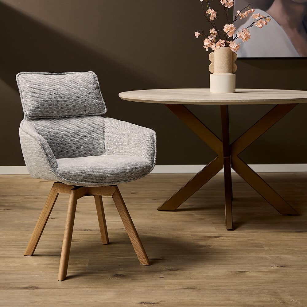 Elegante houten stoel met comfortabel lichtgrijs gestoffeerd zitvlak en rugleuning, gecombineerd met een luxe eettafel en decoratieve bloemenvase in een modern interieur.