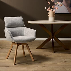 Modern fauteuil met lichtgrijze bekleding en houten poten, gecombineerd met een ronde eettafel met een minimalistisch design en een decoratieve vaas met roze bloemen, passend bij een eigentijdse woonstijl.