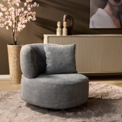 Comfortabele moderne fauteuil in lichtgrijze stof, passend in een eigentijds interieur, gecombineerd met sierkussen voor extra zitcomfort en stijl.