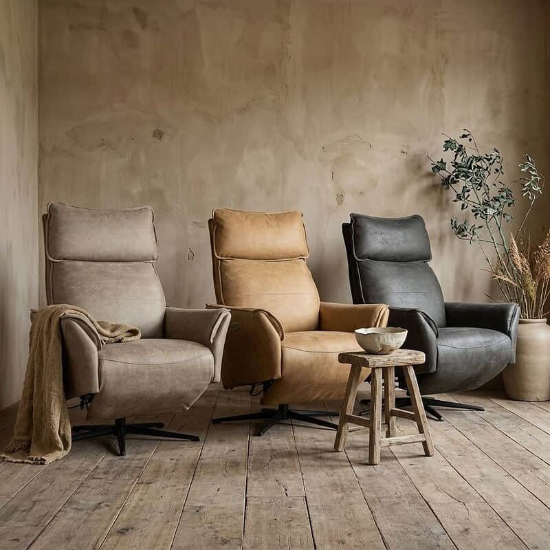 Drie stijlvolle relaxfauteuils van Mokana Meubelen in beige, bruin en zwart, geplaatst in een minimalistische woonkamer met houten vloer en decoratieve planten.