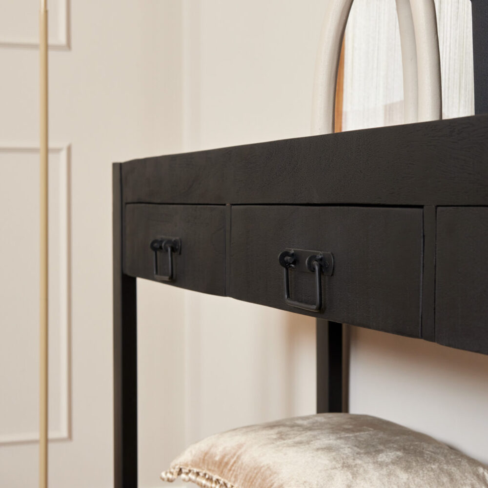 Ruwe zwarte houten kaptafel met lade en metalen handgrepen in een moderne slaapkamer setting.