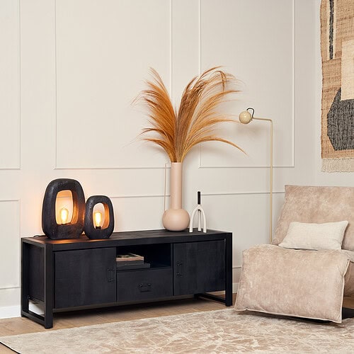 Zwarte houten tv-meubel met twee lades en open vakken, decoratief met sfeervolle lampen en grote vaas met beige decoratie, in een stijlvol, modern interieur.