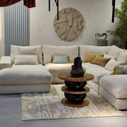 Elegante witte stoffen hoekbank met sierkussens, centrale salontafel met hout en zwarte details, stijlvolle muurdecoratie en groene planten, perfect voor een modern en warm interieur.