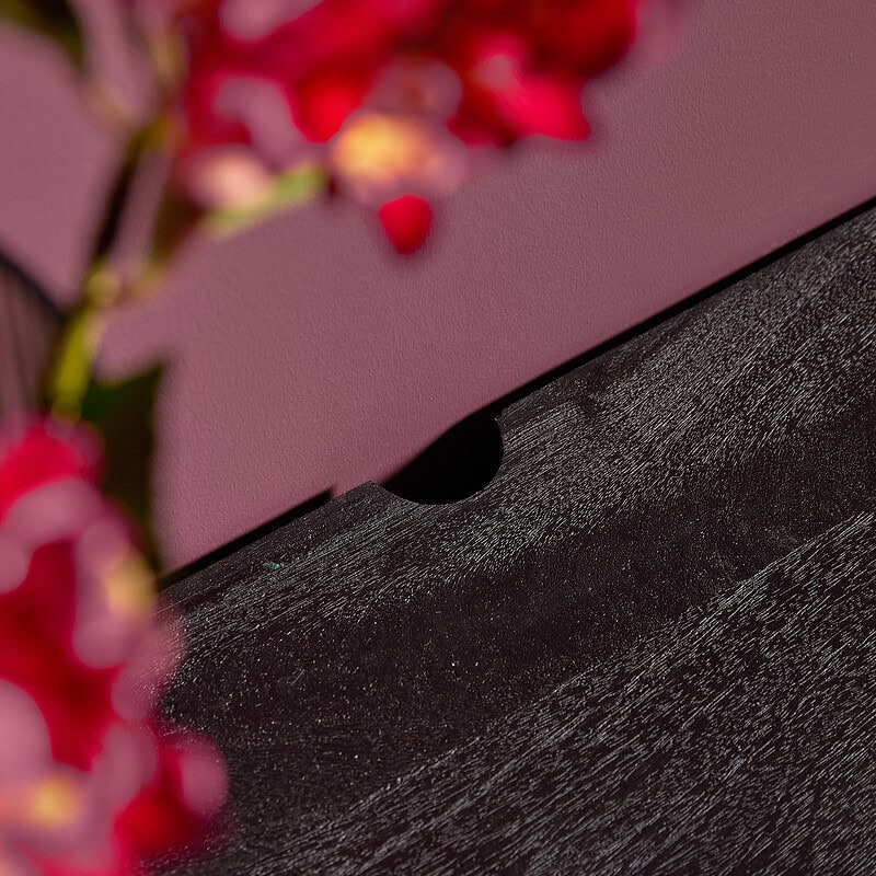Zwart houten meubel met zachte houtstructuur en een viltlaag, gefotografeerd met een roze achtergrond en rode bloemen op de voorgrond, perfect voor moderne en stijlvolle interieurdesigns.