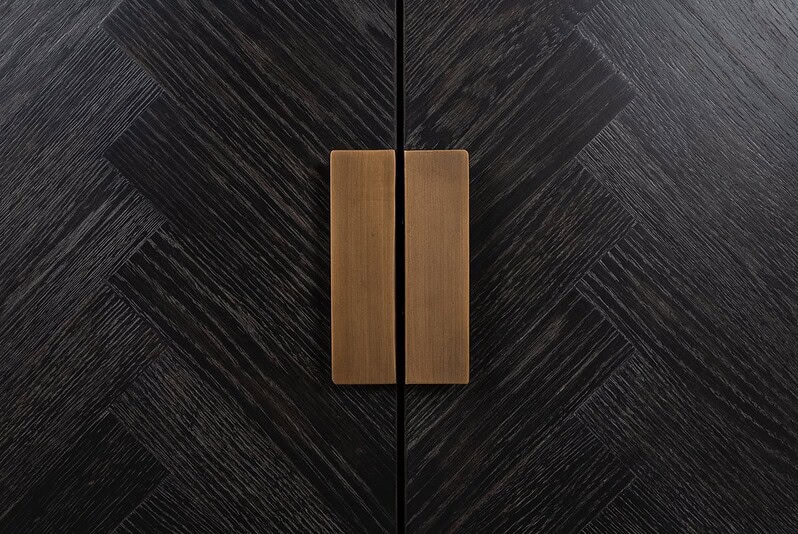 Minimalistisch houten kastdeur met zwarte fineerafwerking en messing handgrepen, stijlvolle en moderne meubels van Mokana Meubelen.