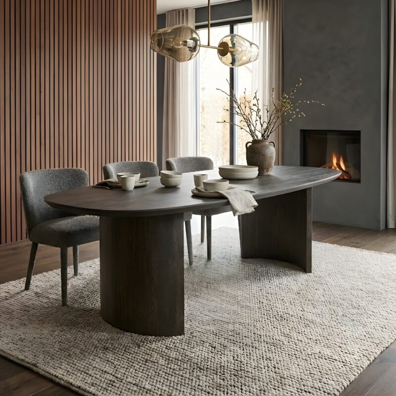 Ovale eettafel Nout van massief eikenhout met donkere Rubio Monocoat afwerking en robuuste houten kolompoten in een moderne luxe eetkamer