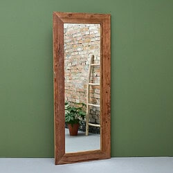 Elegante houten staande spiegel met een rustieke afwerking, geplaatst tegen een groene muur, met een plantenpot en ladder op de achtergrond.