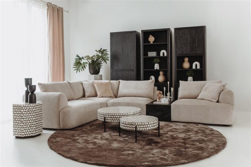 Zwart houten boekenkasten en beige hoekbank in een modern woonkamer met decoratieve accessoires en een ronde bruine vloerkleed.