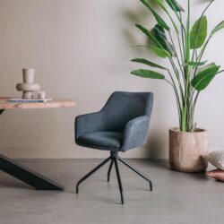 Zwarte bureaustoel met armleuningen en metalen onderstel, geplaatst in een modern interieur met een grote groene plant en een houten tafel.