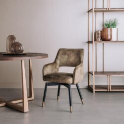 Zitstoel van Mokana Meubelen met een zachte, beige bekleding en elegante zwarte poten met goudaccenten, geplaatst in een modern interieur met een houten tafel en open boekenkast.