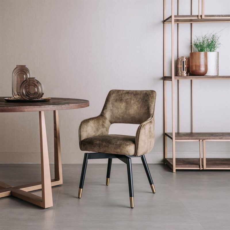 Zitstoel van Mokana Meubelen met een zachte, beige bekleding en elegante zwarte poten met goudaccenten, geplaatst in een modern interieur met een houten tafel en open boekenkast.