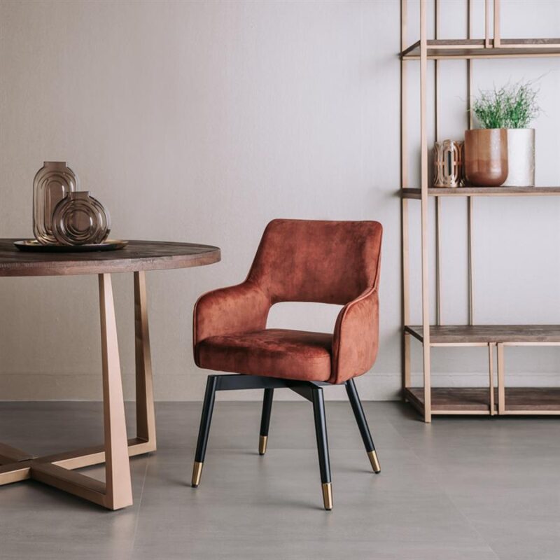 Zachte stoffen eetkamerstoel met elegante zwarte poten en gouden details, geplaatst in een modern interieur met houten meubels en decoratieve accessoires.