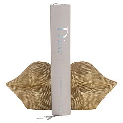 Een boek met de titel "Dior" staat tussen een gouden lipvormige decoratie, perfect voor een luxe interieur of modieuze setting.