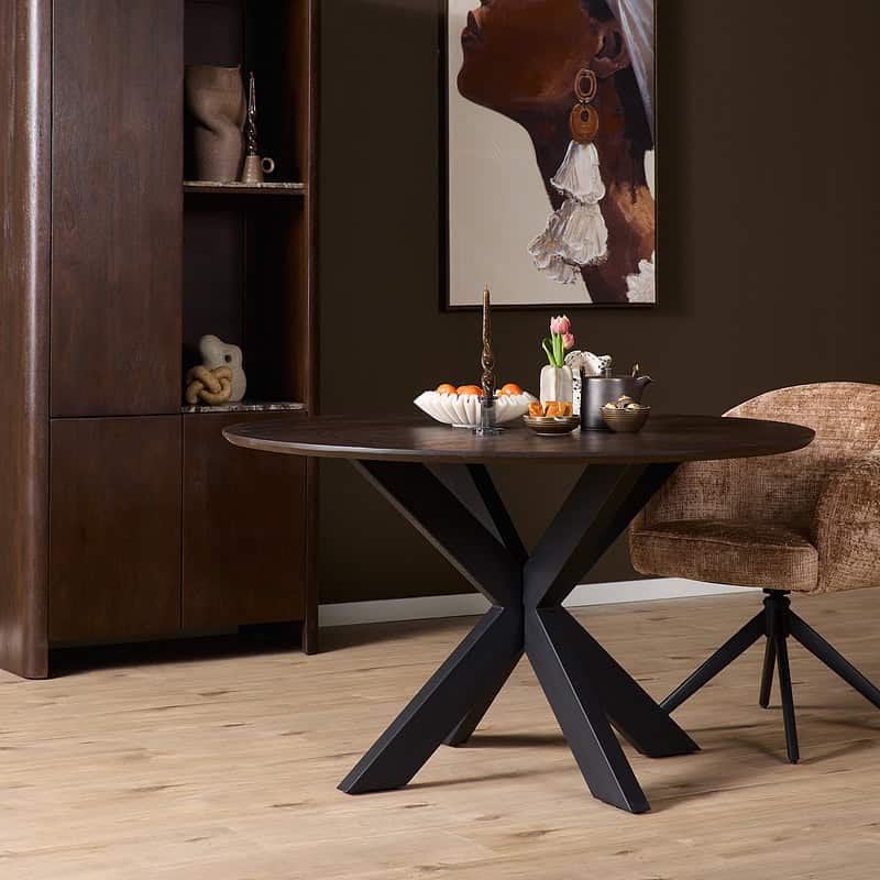 Eiken eettafel Ferris rond 110 cm in donkerbruin, perfect voor gezellige diners en bijeenkomsten. Robuust en stijlvol ontwerp met een unieke voetstructuur, ideaal voor moderne en landelijke interieurs.