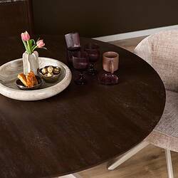 Eettafel Madison Brown met ronde vorm, 130 cm, met zandkleurige poot, afgebeeld met decoratieve glazen en bloemen.