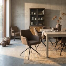 Zwart houten eettafel met moderne stoffen stoelen in een gezellige, minimalistische eetkamer met natuurlijke decoraties en een vintage kast op een betonnen muurachtergrond.