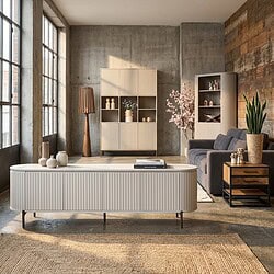 Moderne woonkamer ingericht met stijlvolle Mokana meubels, inclusief een wit dressoir, boekenkast en comfortabele bank, in een industrieel interieur met grote ramen en natuurlijke lichtinval.