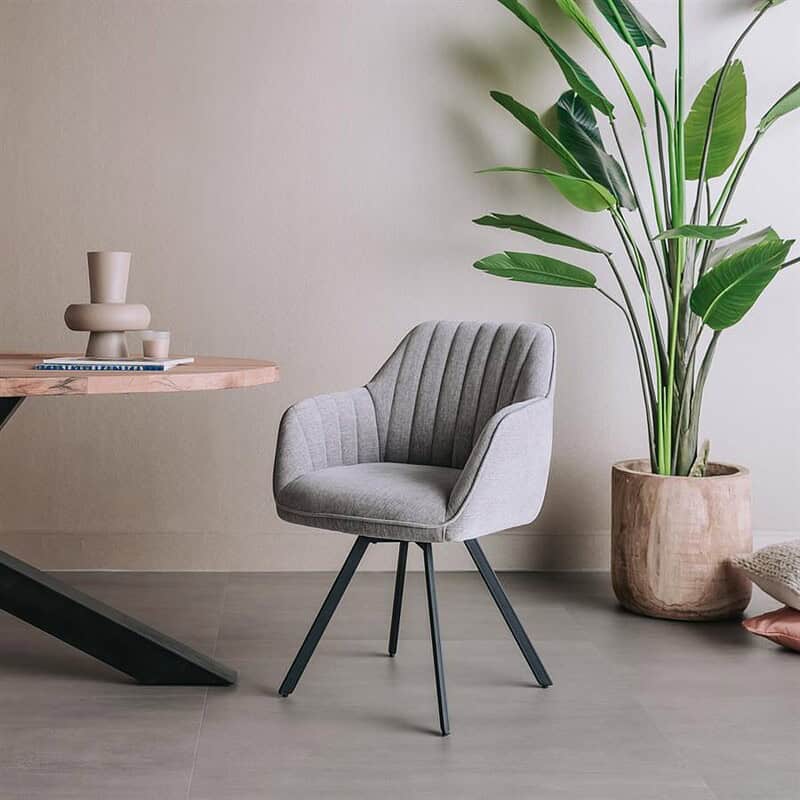 Moderne Bruno armstoel met draaibare functie, bekleed met Nature stof 452 in blauwgrijs, geplaatst in een minimalistische interieursetting met een grote groene plant.