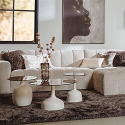 Ein Sofa aus einem hellen, bequemen Stoff mit Kissen, kombiniert mit drei einzigartigen Couchtischen und stilvollen Accessoires für eine moderne Einrichtung.