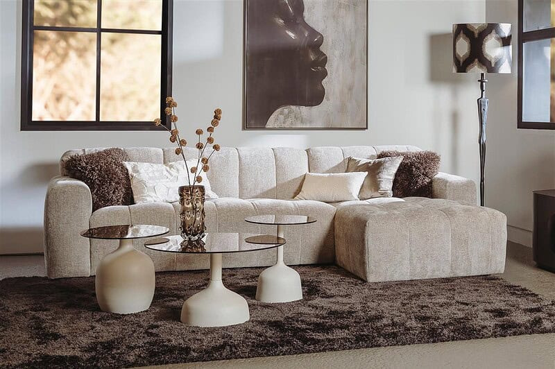 Ein Sofa aus einem hellen, bequemen Stoff mit Kissen, kombiniert mit drei einzigartigen Couchtischen und stilvollen Accessoires für eine moderne Einrichtung.
