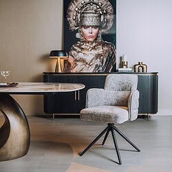Moderne woonkamerinrichting met een comfortabele, lichtgrijze fauteuil en een elegante eettafel, aangevuld met decoratieve accessoires en kunstwerken voor een luxe uitstraling.