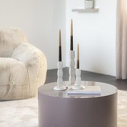 Ein gemütliches Interieur mit einem runden Couchtisch und Kerzenständern in einem hellen, minimalistischen Wohnzimmer.