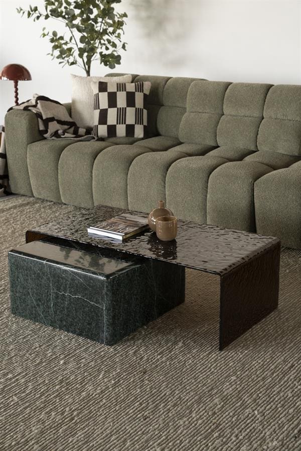 Ein modernes grünes Sofa mit gepolsterten Kissen und Zierkissen im Wohnzimmer, kombiniert mit einem Couchtisch aus schwarzem Marmor und einem Pflanzkübel.