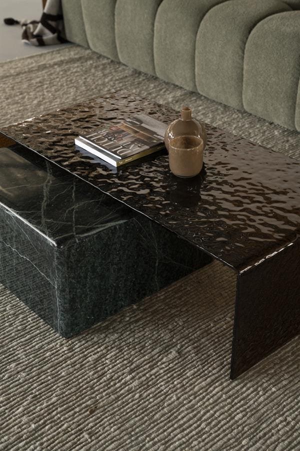 Ein eleganter Couchtisch aus schwarzem Marmor mit glänzender Oberfläche, platziert in einem stilvollen Wohnzimmer mit einem grünen Sofa und einem weichen Teppich. Perfekt für eine luxuriöse Einrichtung.