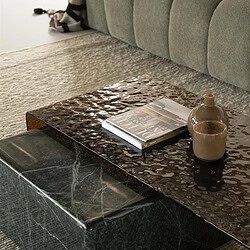 Moderner Couchtisch aus grünem Marmor mit einem Buch und Keramikdekorationen, platziert in einem stilvollen Wohnzimmer mit einem grünen Sofa und einem weichen Teppich.