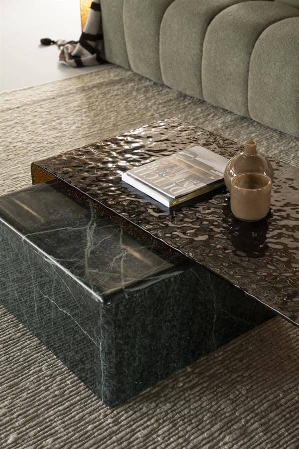 Moderner Couchtisch aus grünem Marmor mit einem Buch und Keramikdekorationen, platziert in einem stilvollen Wohnzimmer mit einem grünen Sofa und einem weichen Teppich.