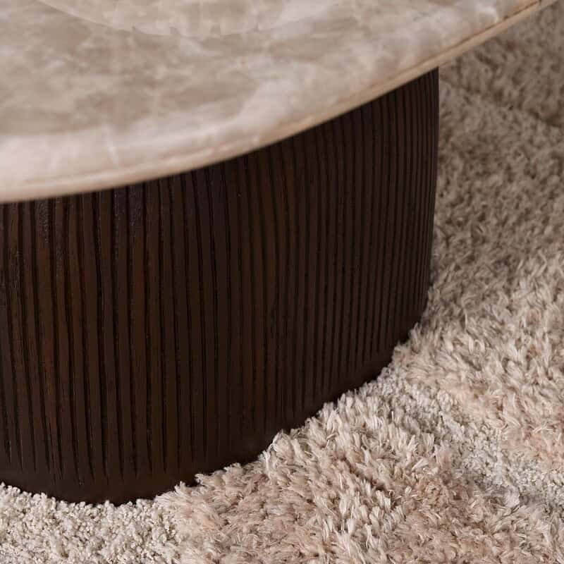 Close-up van de houten salontafel Noel van Mokana, met een ronde vorm en een natuurlijke afwerking, geplaatst op een zachte, beige tapijtvloer.