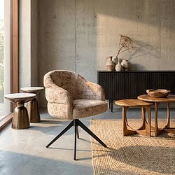 Moderne eetkamerstoel Bella in cinnamon stof met zwart onderstel en armleuningen, geplaatst in een stijlvolle woonkamer met natuurlijke lichtinval.