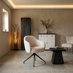 Moderne woonkamer met comfortabele witte fauteuil, zwart bijzettafeltje, witte kast en decoratieve elementen zoals een vaas met droogbloemen en een lamp, perfect voor een gezellige sfeer.