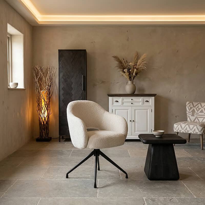 Moderne woonkamer met comfortabele witte fauteuil, zwart bijzettafeltje, witte kast en decoratieve elementen zoals een vaas met droogbloemen en een lamp, perfect voor een gezellige sfeer.