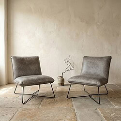 Mokana Meubelen - Moderne fauteuils in minimalistische setting Twee moderne fauteuils met zachte bekleding en zwart metalen frame, geplaatst in een minimalistische woonkamer met een neutrale muur en een decoratieve vaas met takken.