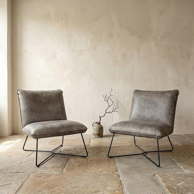 Mokana Meubelen - Moderne fauteuils in minimalistische setting Twee moderne fauteuils met zachte bekleding en zwart metalen frame, geplaatst in een minimalistische woonkamer met een neutrale muur en een decoratieve vaas met takken.