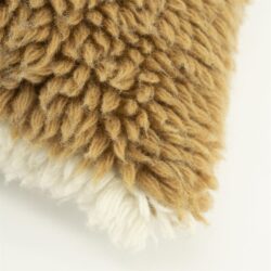 Close-up van een kussen met een wollen textuur in beige en wit, perfect voor een gezellige woonkamer of slaapkamer.
