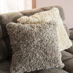 Drie fluffy sierkussens in neutrale tinten op een moderne bank, perfect voor comfort en stijl in je woonkamer.
