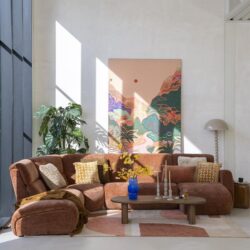Gezellige woonkamer met een grote, comfortabele bank, kleurrijke kussens, een houten salontafel en een opvallend kunstwerk aan de muur, ingericht met Mokana meubelen.