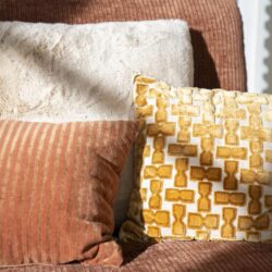 Gezellige bank met drie kussens in verschillende texturen en kleuren, perfect voor een moderne woonkamer.