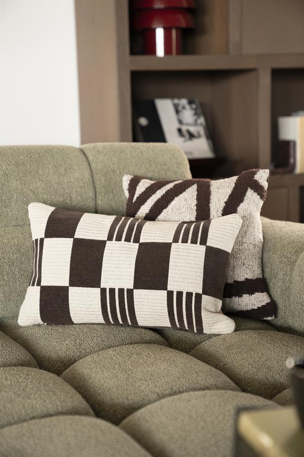 Comfortabele groene bank met zwart-wit gestoffeerde kussens, geplaatst in een stijlvolle woonkamer met houten boekenplank en decoratieve accessoires.