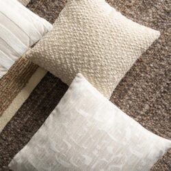 Twee decoratieve kussens op een tapijt in een woonkamer, met een beige en een witte kussen, perfect voor een gezellige en stijlvolle zithoek.