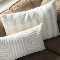 Kussen met beige en witte strepen en patronen, geplaatst op een comfortabele bank. Perfect voor een stijlvolle en gezellige woonkamer.
