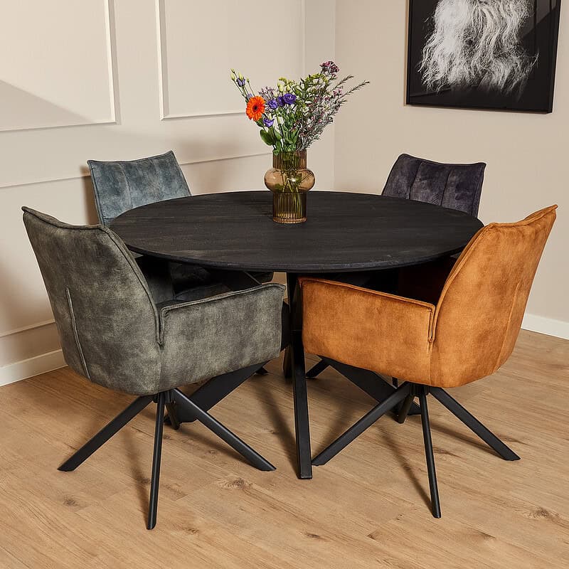 Drie velvet eetkamerstoelen met armleuningen in blauw, grijs en oranje rondom een zwart eettafel, in een moderne eetkamer met witte wand en houten vloer.